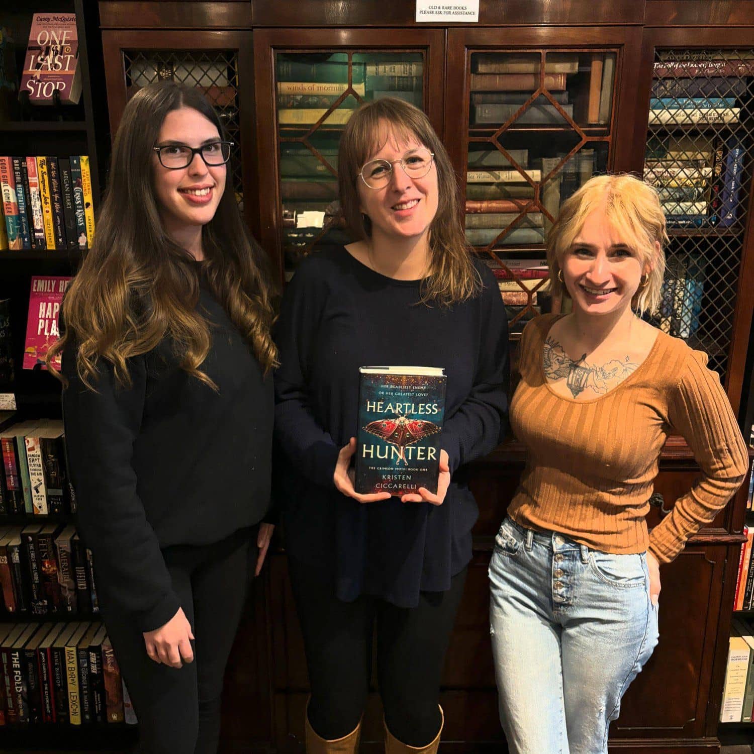 Caitlin, Taylor, and Kyra holding a hardcover romantasy.